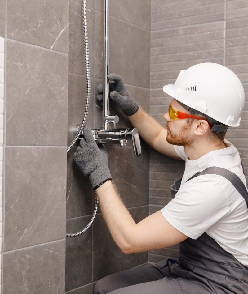 Plumber installing water taps shower stall, work in bathroom.