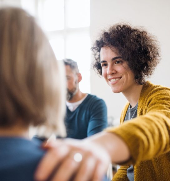 Serious men and women sitting in a circle during group therapy, supporting each other.